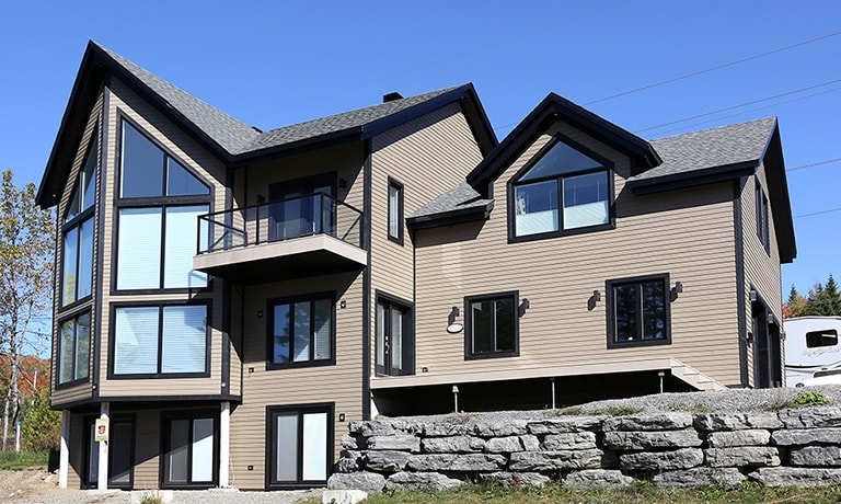 Maison moderne à plusieurs versants avec toiture en bardeaux d’asphalte, montrant des lignes de toit complexes, pignons accentués et grande fenestration, idéale pour des projets de couverture résidentielle haut de gamme.
